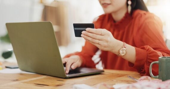 Female holding a credit card in front of a laptop.